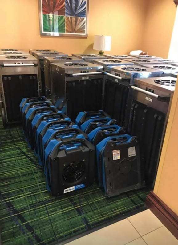 Room filled with dehumidifiers and air movers on patterned carpet