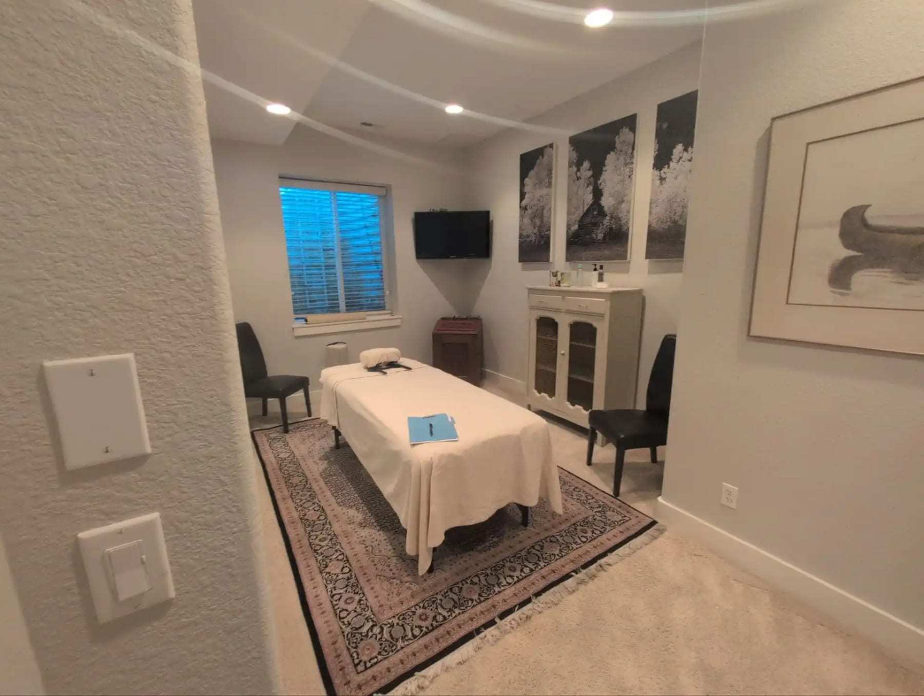 Spa treatment room with a massage table, chairs and framed prints